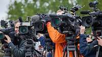 Presseinformationen Journalisten stehen mit ihren Kameras und ihren Stativen nebeneinander. Alle Objektive schauen in eine Richtung.