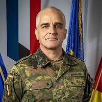 Ein deutscher Oberst schaut in die Kamera, hinter ihm Flaggen.