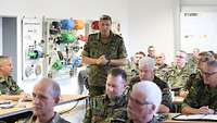 Soldaten sitzen im Feldanzug in einem Unterrichtsraum. Ein General steht in ihrer Mitte. 