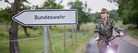 Eine Soldatin unterwegs zu einer Dienststelle der Bundeswehr. Eine Soldatin fährt auf einem Fahrrad an einem Schild mit der Aufschrift „Bundeswehr“ vorbei.