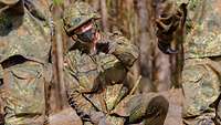Ein Soldat kniet und erläutert neben ihm stehenden Soldaten sein Vorgehen.