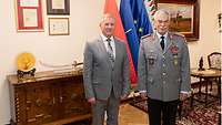Ein Soldat und ein Mann stehen nebeneinander in einem Raum, beide lächeln in die Kamera