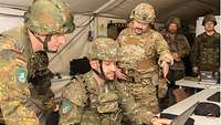 Drei Soldaten aus verschiedenen Nationen. Der Mittlere sitzt an einem Computer und erhält Anweisungen vom Hinteren.