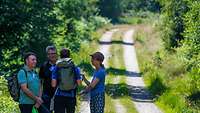 4 Personen stehen im Kreis auf einem Feldweg und unterhalten sich.