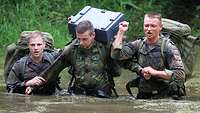 Drei Soldaten waten in Uniform mit Gepäck durch Wasser.