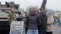 Gäste unterhalten sich mit einem Soldaten. Im Hintergrund steht ein Schützenpanzer.