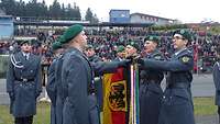 Soldaten stehen nebeneinander und berühren mit ausgestrecktem Arm die hängende Truppenfahne.