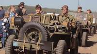 Soldaten in historischen Uniformen sitzen in Militärfahrzeugen aus der Zeit des Zweiten Weltkriegs.