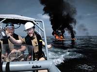 Fregatte Hamburg Operation Atalanta Auf See brennen Reste eines Bootes, im Vordergrund deutsche Marinesoldaten in beigefarbener Arbeitsuniform.