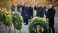 Soldaten und Zivilisten stehen vor den Kränzen und halten inne