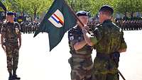 Ein Soldat übergibt einem anderen Soldaten den Wimpel der Deutsch-Französischen Brigade.