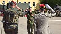 Auf dem Appellplatz grüßen sich drei Soldaten militärisch und stehen sich dabei gegenüber.