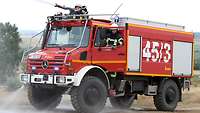 Ein Waldbrandlöschfahrzeug der Bundeswehr steht auf einem Feldweg, zwei Feuerwehrleute sind im Führerhaus.