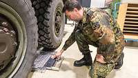 Ein militärisch gekleideter Sachverständiger hockt neben den Rädern eines militärischen Lastwagens und prüft etwas.