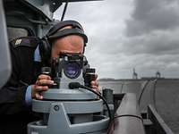 Posten Ausguck Ein Marinesoldat in blauer Arbeitsuniform blickt durch ein optisches Gerät in der Nock eines Schiffes.