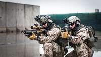 Zwei Soldaten knien auf dem nassen Boden mit der Waffe im Anschlag.