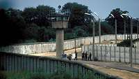 DDR-Grenzsoldaten stehen neben einem Wachturm an der Berliner Mauer.