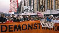 Menschen demonstrieren mit Transparenten vor dem Palast der Republik.