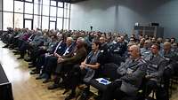 Frauen und Männer sitzen auf Stühlen in einem großen Saal
