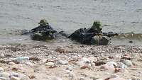 Zwei am Strand im Wasser liegende Kampfschwimmer im Gefechtsanzug mit G36.