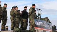 Mehrere Soldaten stehen auf einem Podest, einer spricht in ein Mikrofon.