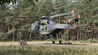 Ein Hubschrauber schwebt in einem Waldstück knapp über dem Boden, unten hocken Soldaten.