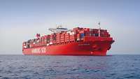 Ein großes Containerschiff mit rotem Rumpf auf See.