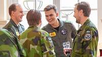 Mehrere Soldaten unterschiedlicher Nationen stehen zusammen, begrüßen sich und lächeln.