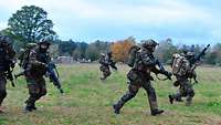 Mehrere Soldaten rennen bewaffnet über freies Gelände.