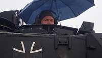 Der Kommandant mit einem Regenschirm in der Kommandantenluke des Panzers.