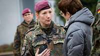Eine Soldatin mit rotem Barett spricht mit einer Frau in einer grauen Winterjacke.
