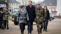 Eine Frau in grauer Winterjacke, ein Mann in schwarzem Mantel und ein Soldat laufen nebeneinander.