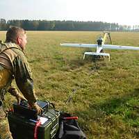 Zwei Soldaten lassen eine Drohne, die auf einer Wiese steht, starten.
