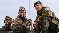 Zwei Soldaten hocken auf einem Panzer, einer erläutert dem anderen etwas.