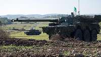 Zwei Panzer stehen versetzt auf einem abschüssigen Gelände.