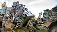 Zwei Soldaten verbinden zwei Fahrzeuge mit einem Abschleppgestänge. Ein Soldat sichert den Vorgang.