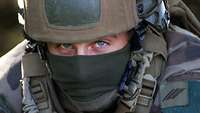 Großaufnahme des Gesichtes eines Soldaten mit Helm und Staubschutztuch über Mund und Nase.