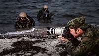 Ein Soldat fotografiert liegend zwei Kampfschwimmer im Wasser