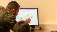 Zwei Soldaten befinden sich vor einem PC und planen auf einer Karte den Einsatz ihres Spähtrupps.