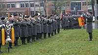 Die Musiker einer Militärkapelle sind auf einer Wiese angetreten und spielen.