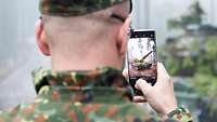 Ein Soldat fotografiert einen Kampfpanzer mit seinem Handy.