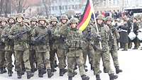 Soldaten marschieren in Formation, dabei tragen sie die deutsche Flagge