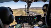 Zwei Piloten sitzen im Cockpit eines Hubschraubers und schauen auf die Rollbahn..