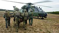 Mehrere Soldaten tragen einen Verwundeten über eine Wiese zu einem Hubschrauber..