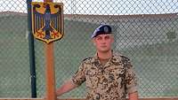 Ein deutscher Soldat steht in Uniform neben einem Schild mit dem deutschen Bundesadler