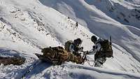 Zwei Soldaten lassen im Schnee eine Trage bergab. Im Hintergrund sieht man die Bergkulisse.