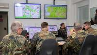 Vier Soldaten blicken auf Computerbildschirme und Monitore, die eine Lagekarte zeigen.