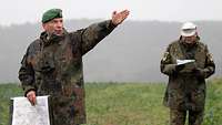 Ein Soldat deutet mit ausgestrecktem linken Arm in die Ferne. Ein Soldat schaut in seine Karte.