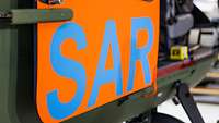 Nahaufnahme einer Hubschraubertür mit dem blauen Schriftzug SAR auf orangefarbenem Grund