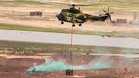 Ein Helikopter ist im Landeanflug, die Außenlast wird mit einem Seil in der Landezone abgesetzt